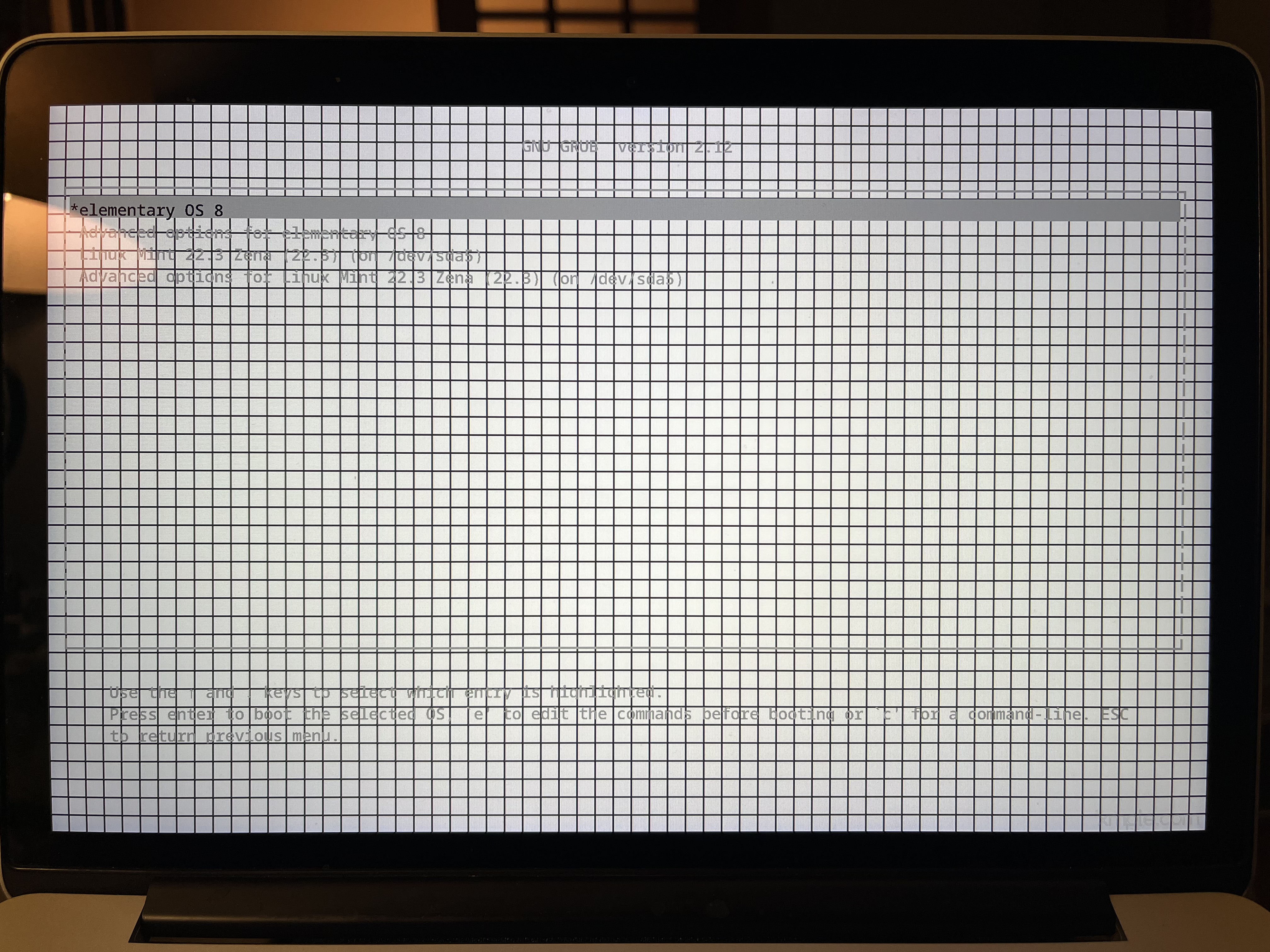 A photo of an old MacBook Pro showing the Grub boot loader on top of a black and white grid
